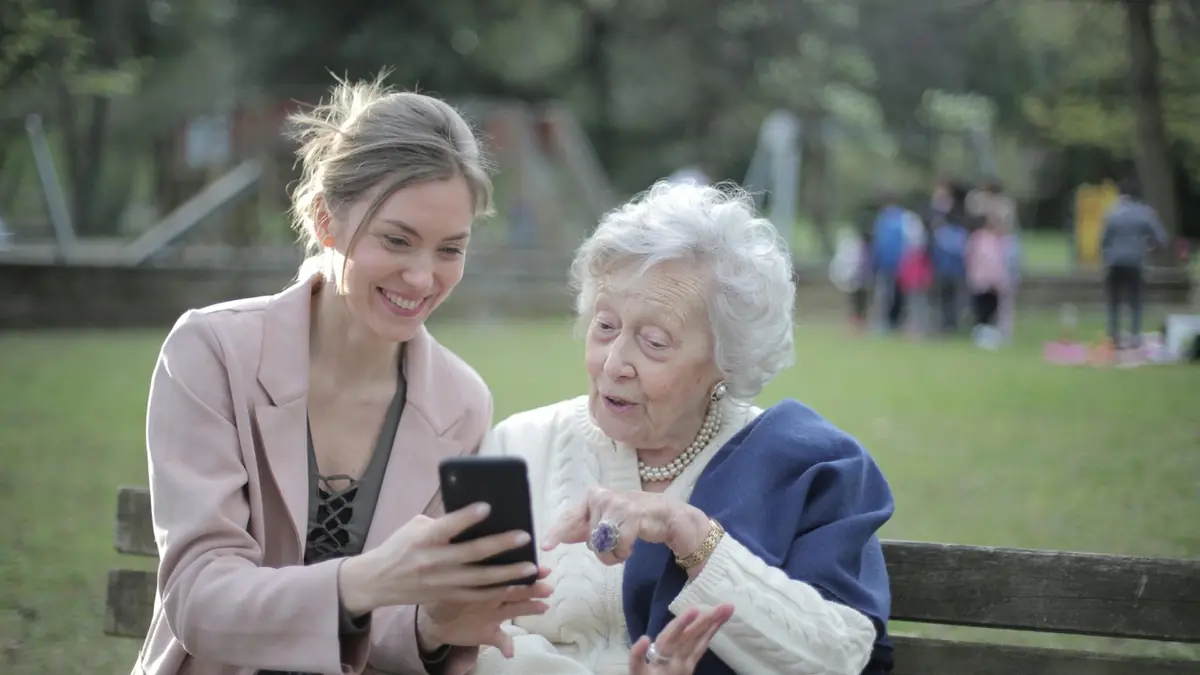 Young woman showing an older woman something on her phone on a park bench