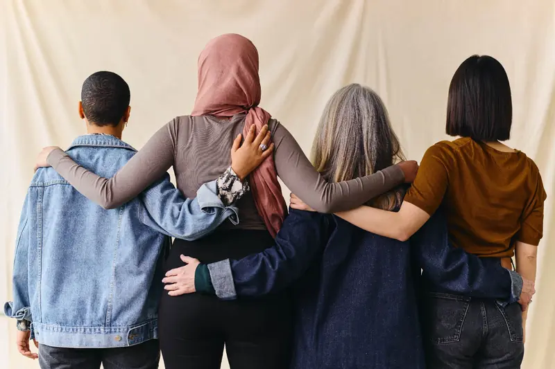 Four people standing together with their arms around each other, seen from behind