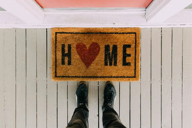 Person standing at a front door mat that reads Home